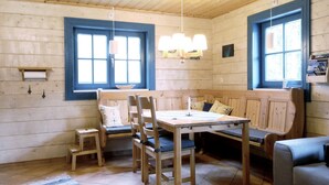 A cozy room with a wooden bench, a table, and chairs. There are two windows with blue frames and a hanging light fixture. - Mountain cabin Ull Oviksfjällen, 4 people (Svenstavik)
