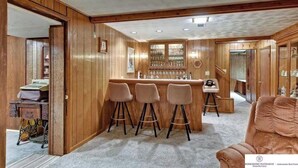 Uma área de bar com lambris de madeira, balcão e três banquetas.