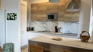 Une cuisine moderne avec des meubles en bois, un pare-feu en marbre, un four à micro-ondes encastré et un îlot central doté de chaises.