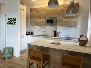 Een moderne keuken met houten kastjes, een marmeren spatwand, een ingebouwde magnetron en een centraal eiland met stoelen.