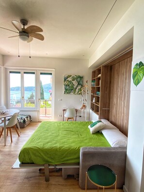 Een slaapkamer met een bed, bureau, stoel, boekenplank en uitzicht op de omgeving.