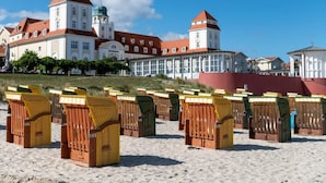 A beach with rows of numbered beach huts and a large historic building in the background. - Exclusive vacation apartment, Residence Margarete, close to the beach, underground parking, sauna (Binz)