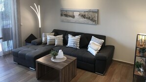 A modern living room with a dark grey sofa, a wooden coffee table, and a painting of a beach scene. - Exclusive vacation apartment, Residence Margarete, close to the beach, underground parking, sauna (Binz)