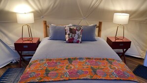 A bed with a striped bedspread, two nightstands with lamps, a colorful floral blanket, and a patterned pillow. - Cozy, Seasonal Geo-Dome with Heat/AC on Private Wilderness Reserve in Gunks.  (Wallkill)