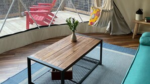 A spacious tent with a wooden table and a hanging chair, a red chair outside, and a teal sofa inside. - Cozy, Seasonal Geo-Dome with Heat/AC on Private Wilderness Reserve in Gunks.  (Wallkill)