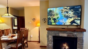 A living room with a fireplace, a dining area with chairs and a table set for four, and a flat-screen TV mounted above the fireplace displaying 'ZenLife'. - Luxury Ski-in/Ski-out 2 BR, Soaring Eagle 207 (Snowshoe)