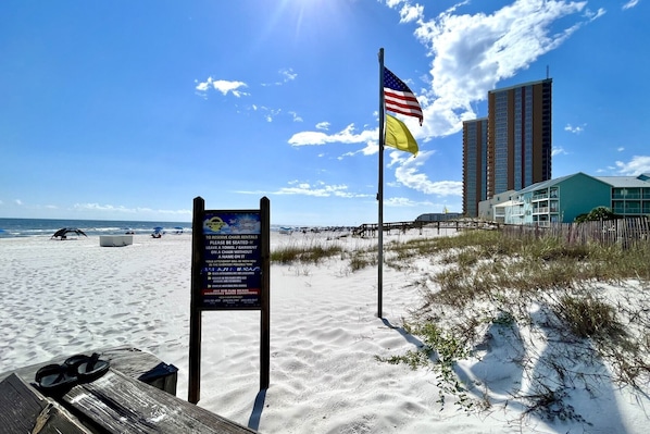 Une plage avec un panneau indicateur, un drapeau et un bâtiment en arrière-plan.