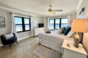 Une chambre à coucher avec un lit, une chaise, une commode, une lampe et une vue sur l’océan.
