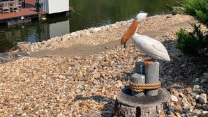 A wooden post with a pelican sculpture, pebbles, and a dock with a shed in the background. - 3 bedroom waterfront home Large dock and great swim area 4 KAYAKS + PADDLEBOAT (Sunrise Beach)