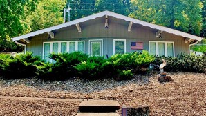 A small, single-story building with a gabled roof, surrounded by dense green foliage. An American flag is displayed on the building's facade. - 3 bedroom waterfront home Large dock and great swim area 4 KAYAKS + PADDLEBOAT (Sunrise Beach)