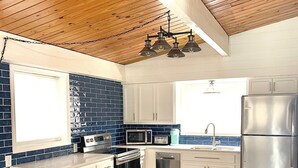 A kitchen with wooden ceiling beams, white cabinets, a stainless steel refrigerator, and a blue-tiled backsplash. - 3 bedroom waterfront home Large dock and great swim area 4 KAYAKS + PADDLEBOAT (Sunrise Beach)