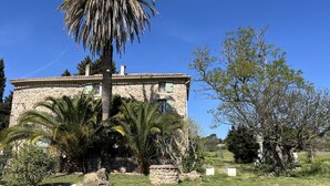 A stone building with a tiled roof, surrounded by palm trees and other vegetation. - Paul à 12 km de la mer (ROQUEBRUNE SUR ARGENS)