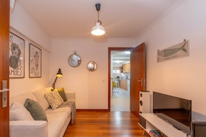 A living room with a sofa, TV, and a hallway leading to a kitchen.