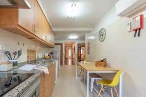 A kitchen with wooden cabinets, a granite countertop, a dining table with yellow chairs, and a clock on the wall.