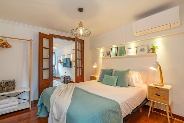 A bedroom with a bed, bedside tables, a wardrobe, and a door leading to another room.
