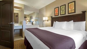 A hotel room with a large bed, a bathroom with a sink and mirror, and three framed pictures on the wall. - Mt. Olympus Water & Theme Park (Wisconsin Dells)
