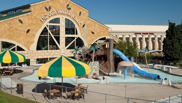 An indoor water park with a large building labeled "INDOOR WATER PARK," a blue slide, and multiple umbrellas. - Mt. Olympus Water & Theme Park (Wisconsin Dells)