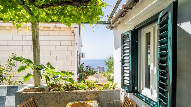 A terrace with a table and chairs, a view of the sea, and a building with green shutters. - Apartment Marija 5 mins away from Old Town (Dubrovnik)