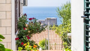 A view of a building with a tiled roof, a balcony with red flowers, and a clear view of the sea in the background. - Apartment Marija 5 mins away from Old Town (Dubrovnik)