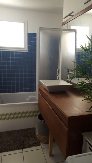 Une salle de bain avec un lavabo blanc, un meuble-lavabo en bois, un miroir, une douche et des murs recouverts de carreaux bleus.