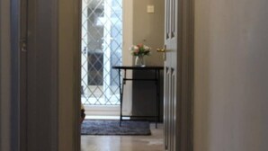 A hallway with wooden flooring leading to a door with a window. There is a small table with a vase of flowers near the door. - LONDON apartment with PRIVATE HOT TUB, SAUNA & GYM! (Rainham)