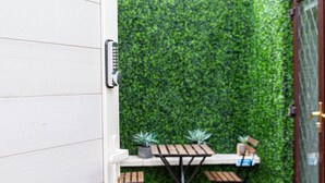 A patio with a wooden table and chairs, a small potted plant, and a green hedge wall. - LONDON apartment with PRIVATE HOT TUB, SAUNA & GYM! (Rainham)