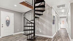 A modern interior with a spiral staircase, wooden floor, and a hallway leading to a door with a stained glass window.