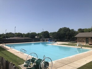 Una piscina con agua azul cristalina, rodeada por una valla y árboles.