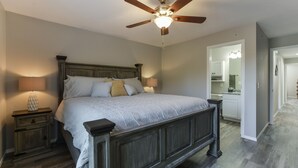 A bedroom with a wooden bed, two bedside tables with lamps, a ceiling fan, and a view into the bathroom. - Accommodates 16! Stylish & Chic! Swim at pool! Close to Lake, SDC & Hwy 76 Strip (Branson)