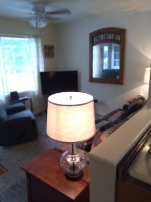 Un salon avec une lampe posée sur une petite table en bois, un canapé, un téléviseur et un miroir accroché au mur.