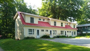 A two-story house with a red roof, surrounded by lush greenery. - Cozy Up-North Townhouse Bungalow (harbor springs)