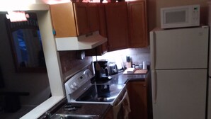 A kitchen with wooden cabinets, a stainless steel sink, a white refrigerator, a microwave, and a stove. - Cozy Up-North Townhouse Bungalow (harbor springs)