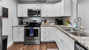 A kitchen with white cabinets, a stainless steel microwave, a stove, and a sink. - 4BDR+Pets OK+Huge Yard+FirePit+3mintoBeach (Rockport)