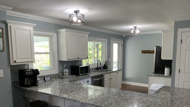 A kitchen with white cabinets, granite countertops, and a central island with bar stools. - Beautiful River front property (Celina)