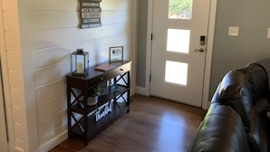 A room with a wooden console table, a door with a frosted glass window, and a dark leather couch. - Beautiful River front property (Celina)