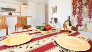 A dining area with a table set for two, a kitchen in the background, and a painting on the wall. - L'Hyppocampe by Interhome (Port Camargue)