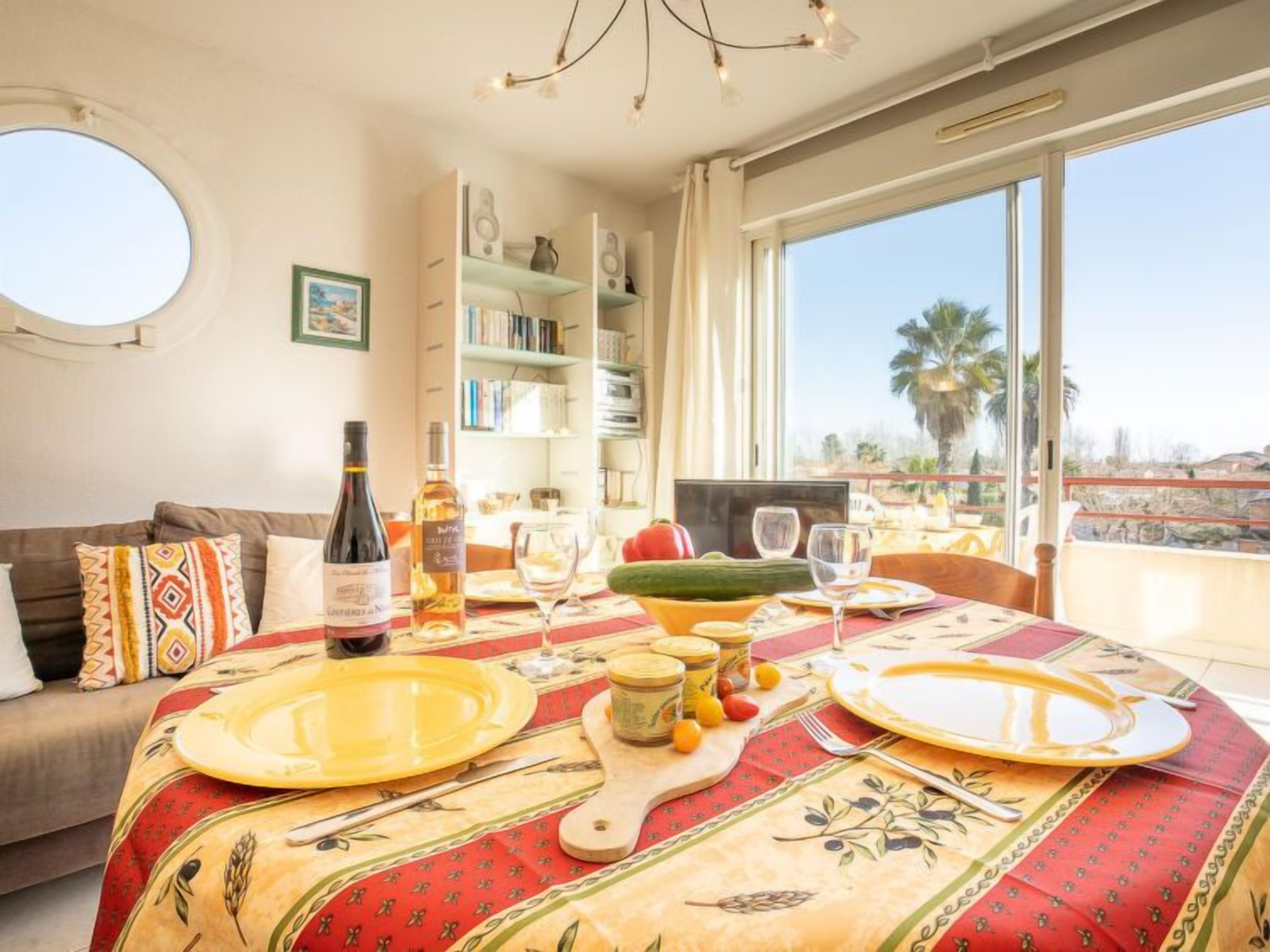 Un comedor con una mesa dispuesta para dos, una botella de vino y una estantería al fondo.