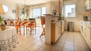 A bright, open-plan living and dining area with a kitchen, large windows, and a view of the city. - L'Hyppocampe by Interhome (Port Camargue)