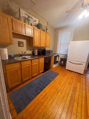 A compact kitchen with wooden cabinets, a microwave, stove, and a refrigerator. - Pet Friendly First Floor 2 Bedroom Apartment (St. Louis)