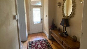 A hallway with a wooden floor, a red and black patterned rug, a wooden console table with a lamp, wall sconces, and a mirror. - Pet Friendly First Floor 2 Bedroom Apartment (St. Louis)