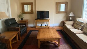 A living room with a wooden coffee table, a sofa, a TV on a stand, and a potted plant. - Pet Friendly First Floor 2 Bedroom Apartment (St. Louis)