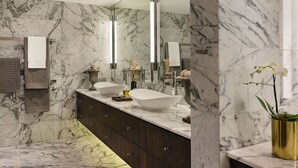 A modern bathroom with marble walls, a large mirror, two sinks, and a potted orchid.
