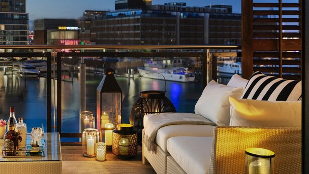 A modern hotel room with a balcony overlooking a marina and cityscape.