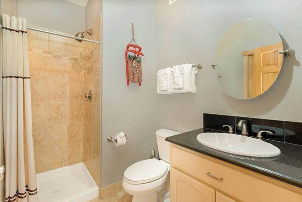 A bathroom with a shower, toilet, sink, and a mirror.