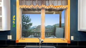 Una cocina con un lavamanos doble, una ventana con marco de madera y vistas a las montañas.