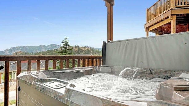 Un jacuzzi en una terraza al aire libre con vistas a montañas y un balcón de madera.