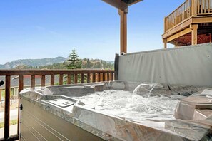 A hot tub on an outdoor deck with a view of mountains and a wooden balcony.