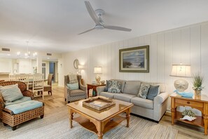 A living room with a dining area, a ceiling fan, and a large window with a view.
