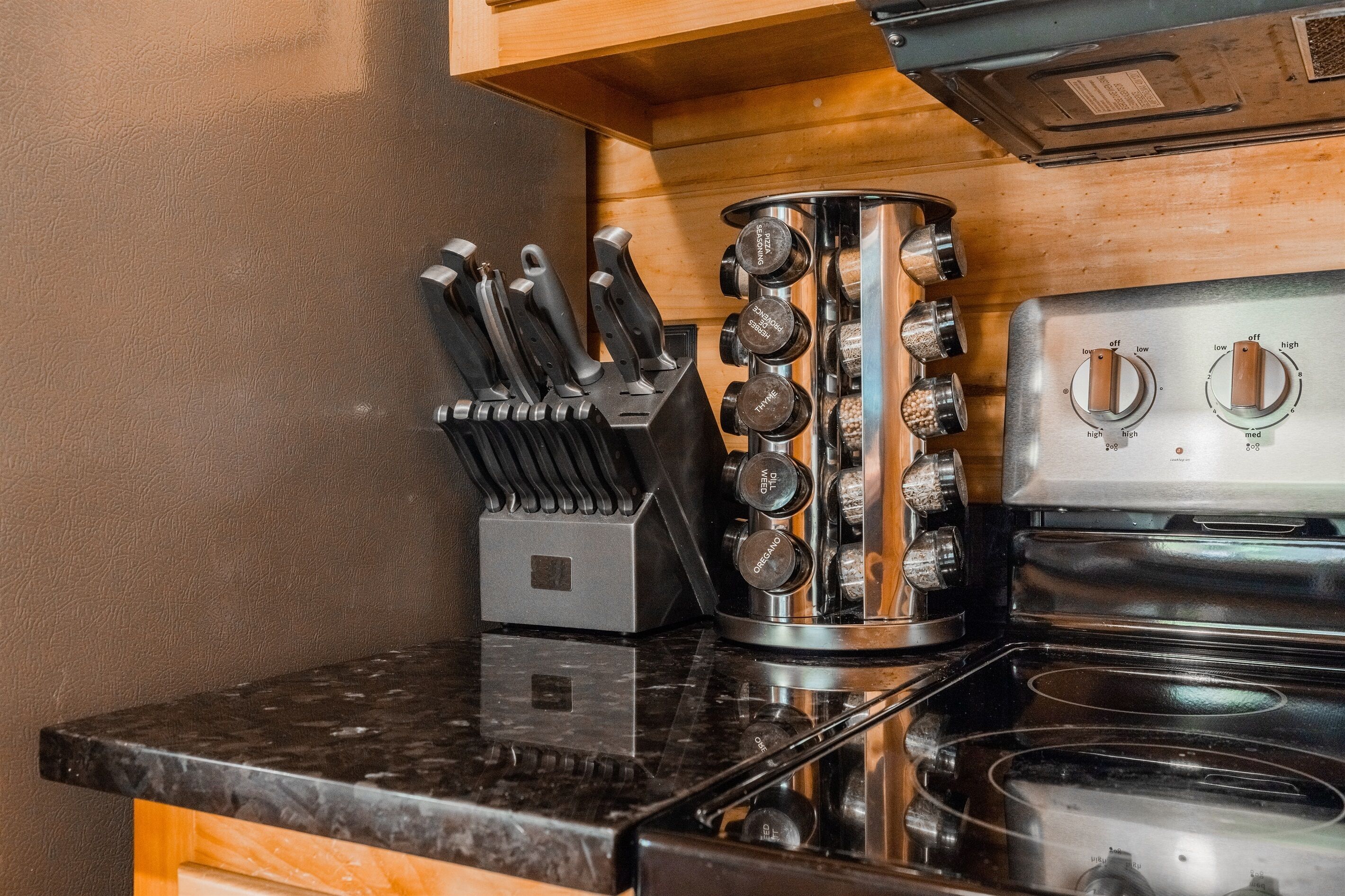 A kitchen with a black granite countertop, stainless steel stove, and a knife block with various knives.