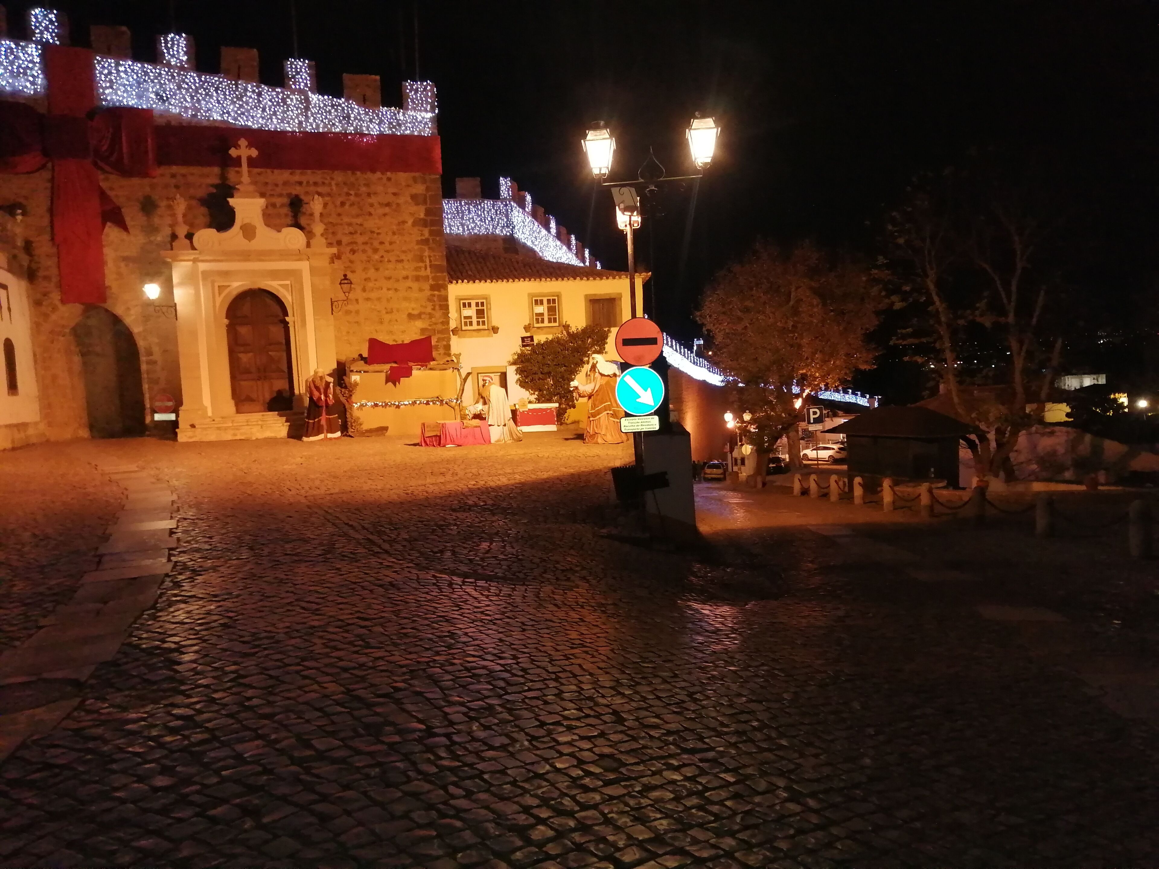 Rua de paralelepípedos à noite, com um edifício histórico com um grande arco e uma faixa vermelha.